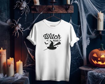 May include: White t-shirt with the text "Witch Please" and a graphic of a witch hat and broom. The shirt is hanging on a metal hanger against a dark blue wooden wall decorated with Halloween-themed items, including spiders, candles, and a carved pumpkin.