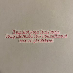 May include: Pink and white sticker with the text "I am not your long term long distance low commitment casual girlfriend".