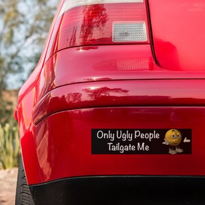 May include: A red car with a bumper sticker that says "Only Ugly People Tailgate Me" with a yellow cartoon face with a frown and a hand gesture.