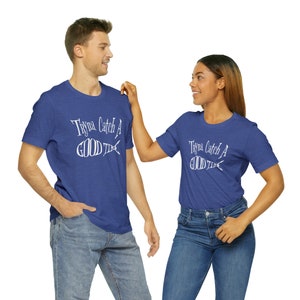 May include: Two people wearing matching blue t-shirts with white text that reads "Tryna Catch A Good Time" and a fish graphic. The shirts are a heather blue color.
