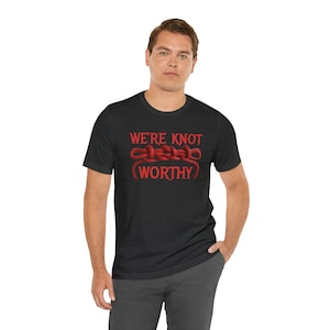 May include: A dark heather grey t-shirt with a red knotted rope graphic and the text "We're Knot Worthy".