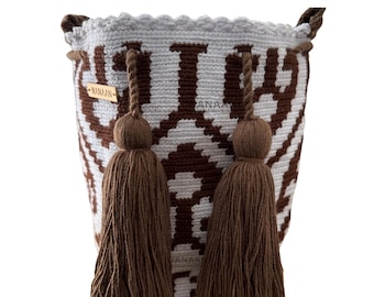 Puede incluir: Un bolso de cubo tejido con un patrón geométrico blanco y marrón. El bolso tiene dos borlas marrones y dos asas. El texto "WANAAN" es visible en una pequeña etiqueta dorada.