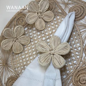 May include: A set of woven flower napkin rings in a natural beige color. The rings are made of natural materials and are perfect for adding a touch of rustic elegance to any table setting.