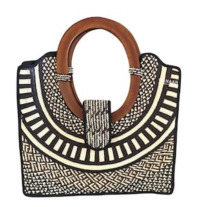 May include: A handcrafted tote bag with a geometric pattern in black and cream. It features a large, circular wooden handle and a matching wooden clasp. The bag's design incorporates a variety of shapes and textures, creating a unique and stylish accessory.