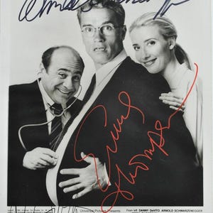 Może przedstawiać: Czarno-białe zdjęcie promocyjne do filmu "Junior" z Dannym DeVito, Arnoldem Schwarzeneggerem i Emmą Thompson. Zdjęcie zawiera autografy i tytuł filmu. Aktorzy są ubrani w garnitury.