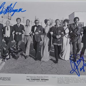 May include: Black and white photograph featuring a group of people, arm in arm, walking down a street. The image is a promotional still for "The Towering Inferno" movie, with signatures in blue ink. Text at the bottom lists the movie's title and credits.