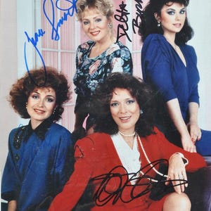 May include: A group photo of four women, each with distinct hairstyles and attire. The women are wearing dresses and blouses in shades of blue and red. The image is signed with blue and black ink.