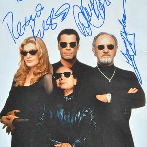 Może przedstawiać: Zdjęcie czterech osób, wszystkie w okularach przeciwsłonecznych, pozujących razem. Obraz jest podpisany niebieskim tuszem. Osoby są ubrane w czarne ubrania. Kobieta po lewej ma blond włosy.