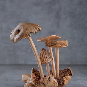 May include: A wooden sculpture of a group of mushrooms with brown caps and stems. The mushrooms are arranged in a cluster on a piece of wood.