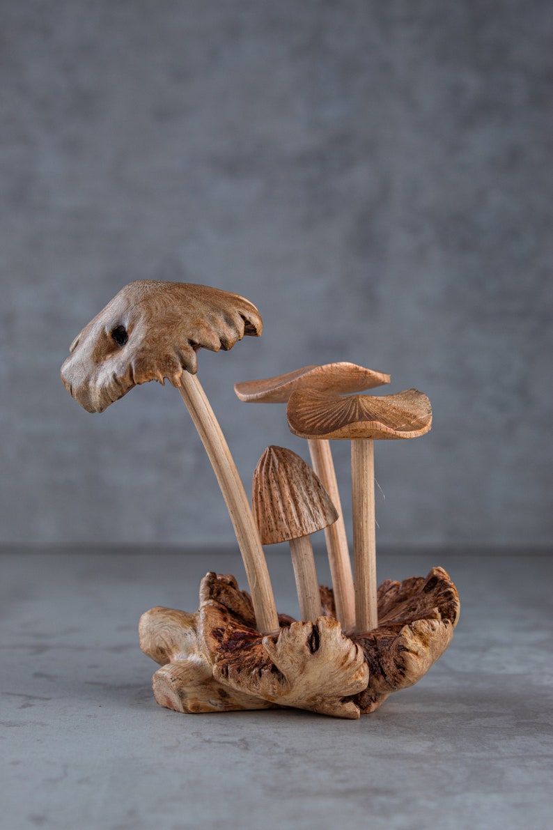 May include: A wooden sculpture of a group of mushrooms with brown caps and stems. The mushrooms are arranged in a cluster on a piece of wood.