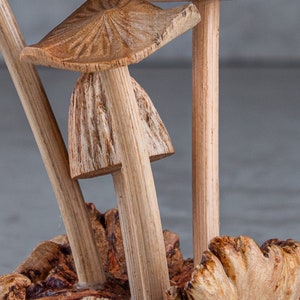May include: A wooden sculpture of three mushrooms with brown caps and stems. The mushrooms are arranged in a cluster and are sitting on a piece of wood.