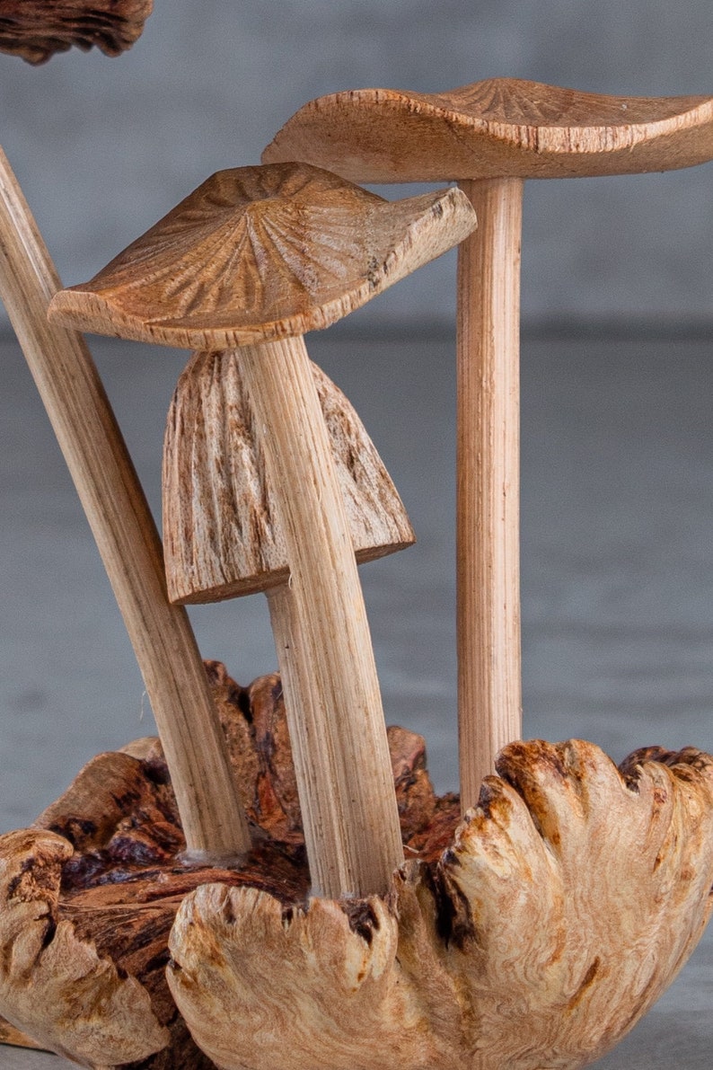 May include: A wooden sculpture of three mushrooms with brown caps and stems. The mushrooms are arranged in a cluster and are sitting on a piece of wood.