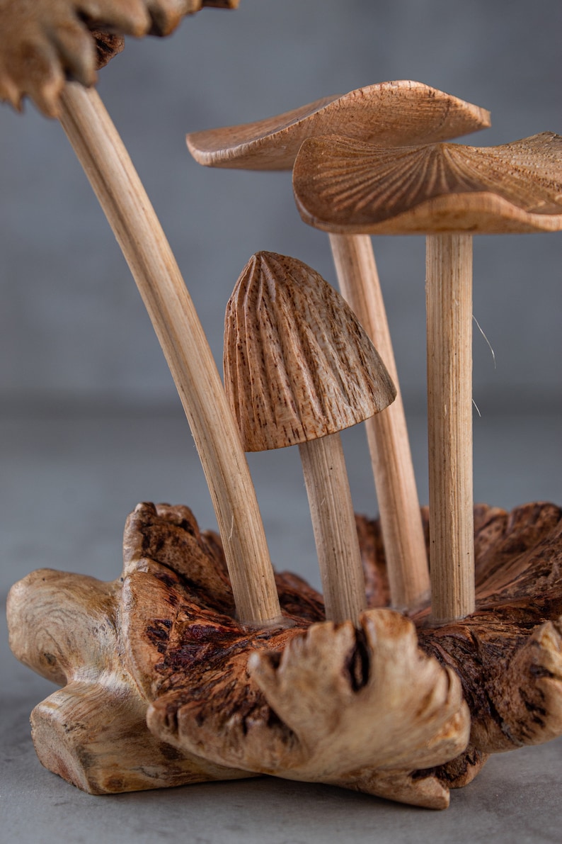 May include: A wooden sculpture of mushrooms with detailed carvings. The mushrooms are arranged in a cluster on a wooden base.