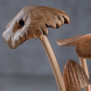 May include: Close-up of a wooden mushroom sculpture with a brown, textured cap and a light brown stem. The sculpture is made to look like a cluster of mushrooms growing together.