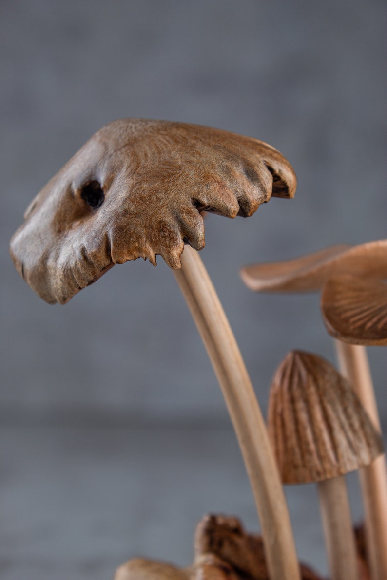 May include: Close-up of a wooden mushroom sculpture with a brown, textured cap and a light brown stem. The sculpture is made to look like a cluster of mushrooms growing together.