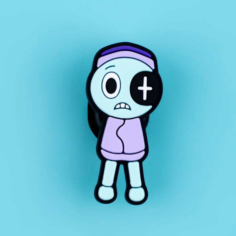 May include: A rubberized shoe charm featuring a cartoon character with light blue skin, a purple headband, and a light purple sweater. The character has one round eye and one black eye patch with a white cross symbol, and a worried facial expression.