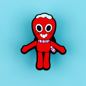May include: A red enamel pin shaped like a cartoon character with a white head topping, large black and white eyes, a wide smiling mouth with two teeth, and a pink and white striped scarf around its neck, outlined in a thick black border.