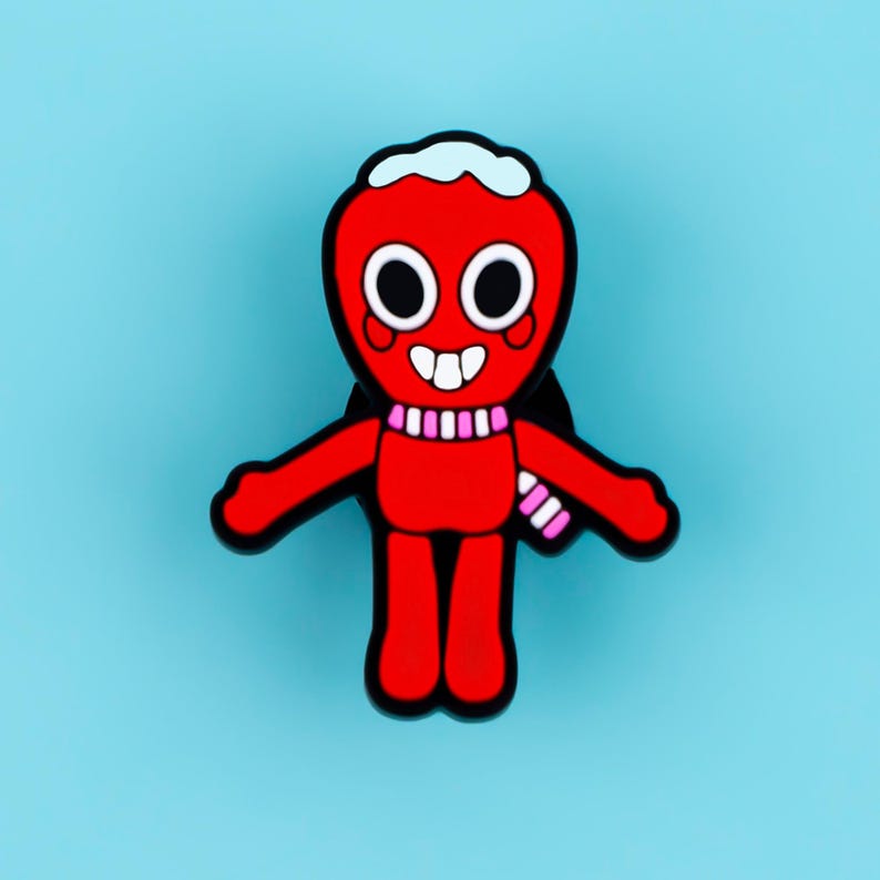 May include: A red enamel pin shaped like a cartoon character with a white head topping, large black and white eyes, a wide smiling mouth with two teeth, and a pink and white striped scarf around its neck, outlined in a thick black border.
