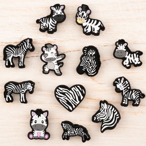 May include: A set of 11 black and white zebra shoe charms. The charms feature different poses of zebras, including a zebra with a heart-shaped body.