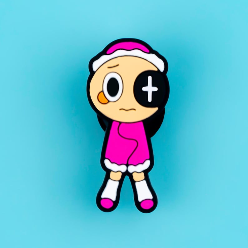 May include: A cartoon character pin featuring a round head with a white hat, one white eye, and one black eye with a white plus sign. The character wears a bright pink coat with white trim, white socks, and pink shoes against a solid blue background.