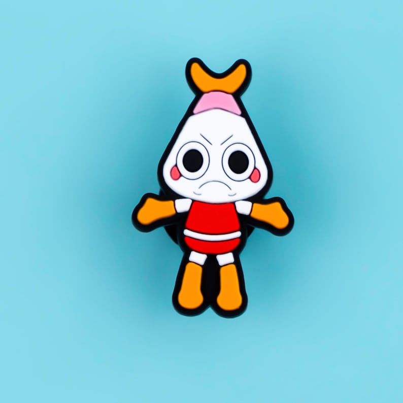 May include: A cartoon character pin featuring a white head with large black eyes, a pink top section, and an orange crest. The figure has a red torso, orange arms, and orange legs, all outlined in black, creating a bold, graphic appearance.