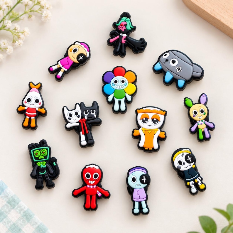 May include: A collection of twelve colorful, cartoon-style shoe charms featuring various whimsical characters, including a rainbow flower, a red creature, a grey robot-like figure, and several stylized humanoid figures with diverse expressions.