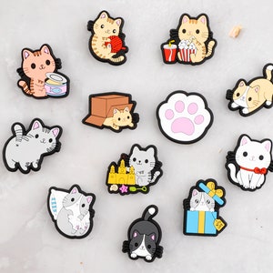 May include: Set of 10 colorful cat-themed charms featuring various activities like eating popcorn, playing with yarn, and sleeping. The charms are made of a soft, flexible material and are perfect for adding a touch of whimsy to your belongings.