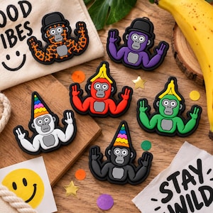 May include: A collection of six colorful rubberized gorilla charms, each featuring a unique accessory like a black bowler hat, a yellow banana peel hat, or a rainbow-striped party hat. The gorillas are depicted with raised arms and peace signs.