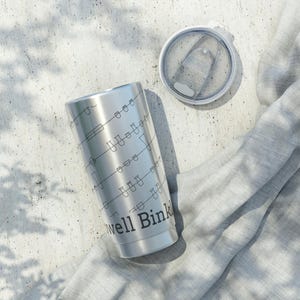 May include: A stainless steel tumbler with a black line art design and the words "Well Bink" printed on the side. The lid is off to the side, and the tumbler is on a light gray surface.