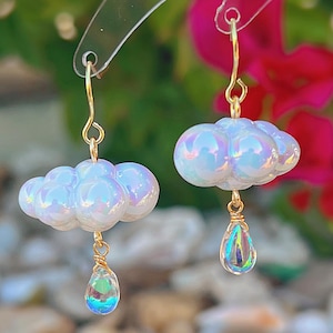 May include: A pair of iridescent white cloud earrings with gold wire and iridescent teardrop crystals hanging from the bottom.