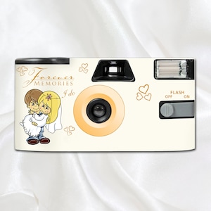 May include: A cream-coloured disposable camera featuring a cartoon couple and the words "Forever Memories I do." The camera has a flash, lens, and viewfinder. Gold hearts decorate the surface of the camera.