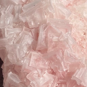 May include: A cluster of pink and white salt crystals. The crystals are translucent and have a rough, textured surface.