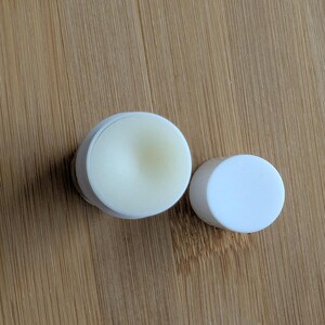 Puede incluir: Dos recipientes redondos blancos, uno con tapa y otro con una sustancia blanca y cremosa en su interior.