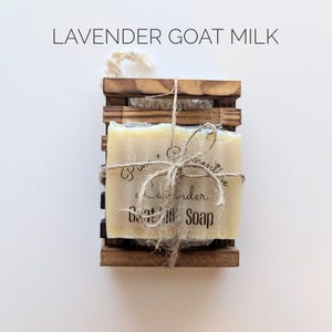 May include: A wooden soap holder with a bar of lavender goat milk soap. The soap is wrapped in clear cellophane and tied with twine. The text "Lavender Goat Milk Soap" is visible on the soap.