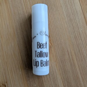 Puede incluir: Tubo blanco de b&aacute;lsamo labial con texto negro que dice "Lime + Clementine Beef Tallow Lip Balm".