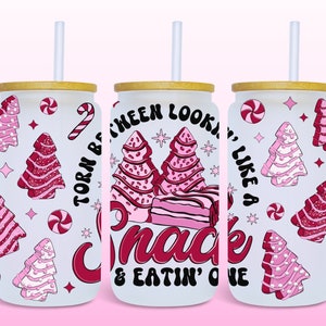 May include: Three white tumblers with pink and red Christmas tree designs and the text "Torn between lookin' like a snack & eatin' one". Each tumbler has a bamboo lid and a clear plastic straw.