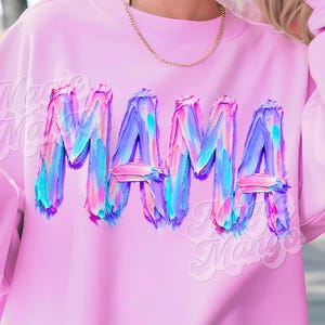May include: A pale pink sweatshirt featuring the word "MAMA" in a vibrant, textured design. The letters are rendered in shades of blue, purple, and pink. The sweatshirt has long sleeves and a round neck.