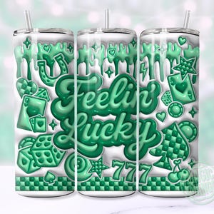 May include: A white tumbler with a green "Feelin' Lucky" design. The design includes dice, playing cards, hearts, stars, and a horseshoe. The tumbler has a silver lid and a straw.