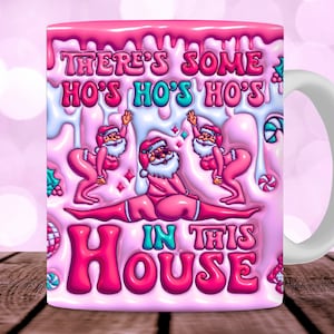 May include: Pink ceramic coffee mug with a white handle. The mug has a pink and white dripping glaze design with a cartoon image of Santa Clauses. The text on the mug reads "There's some ho's ho's ho's in this house".