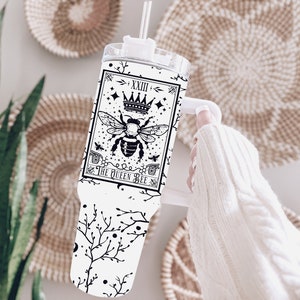 Puede incluir: Un vaso de acero inoxidable blanco con un diseño en blanco y negro que presenta una abeja con una corona y el texto "The Queen Bee".