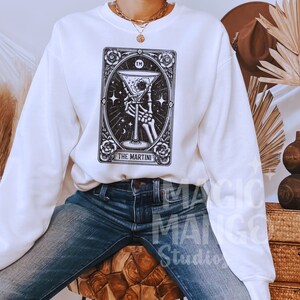 May include: White sweatshirt with a black and white illustration of a tarot card with the text "The Martini" and "TM" on the card.