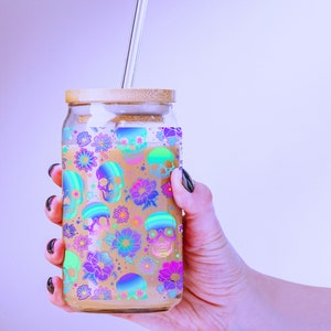 May include: A glass jar with a bamboo lid and a glass straw. The jar is filled with a light brown liquid and has a colourful pattern of skulls and flowers.