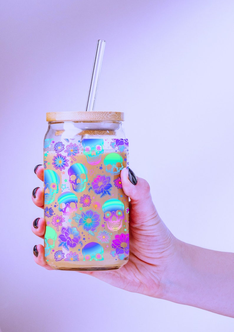 May include: A glass jar with a bamboo lid and a glass straw. The jar is filled with a light brown liquid and has a colourful pattern of skulls and flowers.