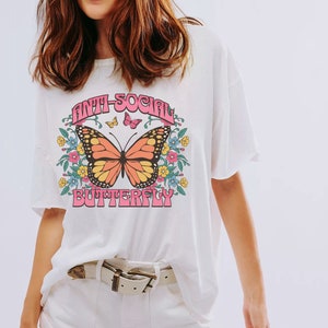 Peut inclure: T-shirt blanc avec un motif de papillon et le texte "Anti-Social Butterfly" en lettres roses.