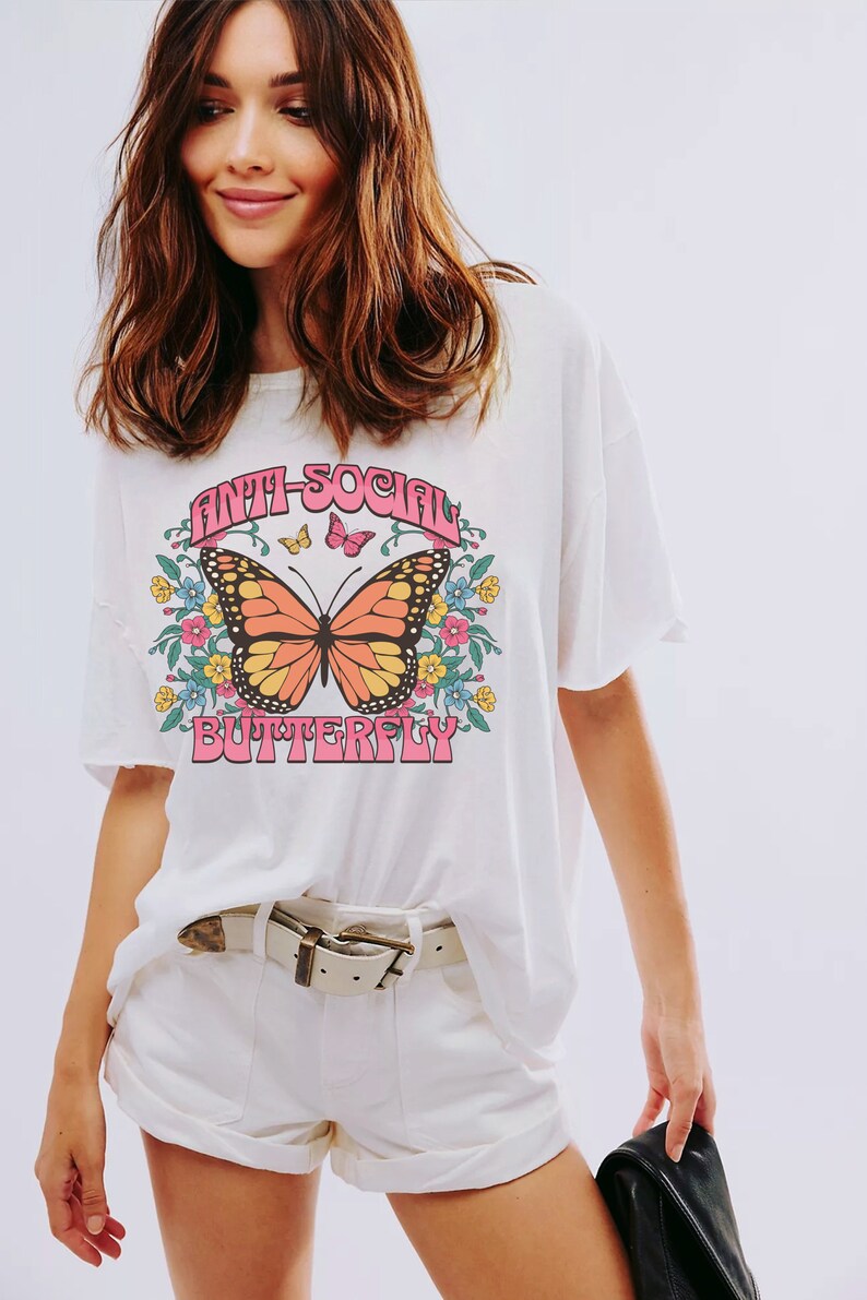 Peut inclure: T-shirt blanc avec un motif de papillon et le texte "Anti-Social Butterfly" en lettres roses.