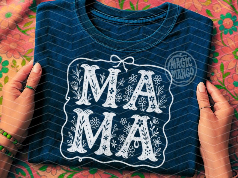 Puede incluir: Una camiseta azul oscuro con un dise&ntilde;o blanco que dice "MAMA" en una fuente decorativa con acentos florales.