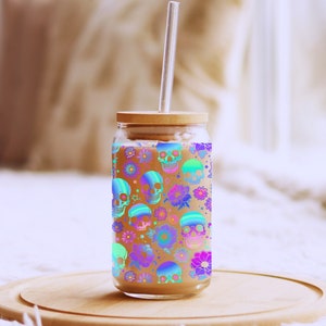 May include: A glass drinking jar with a wooden lid and a clear drinking straw. The jar has a colourful pattern of skulls and flowers.