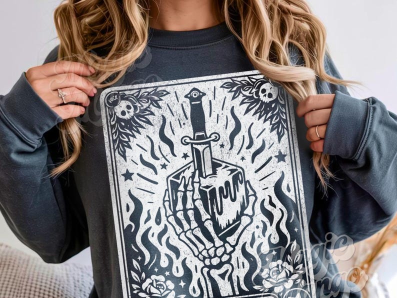 Pu&ograve; includere: Felpa grigio scuro con grafica in bianco e nero. La grafica raffigura una mano scheletrica che tiene un cubo trafitto da un pugnale, circondato da fiamme, stelle ed elementi floreali. Il design ha un'estetica vintage e gotica.