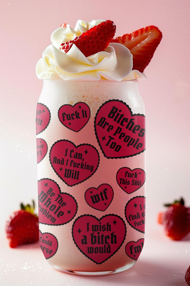 Puede incluir: Un vaso con una bebida rosa, cubierto con crema batida y rodajas de fresa. El vaso est&aacute; decorado con pegatinas rosas en forma de coraz&oacute;n con texto negro, incluyendo frases como "Fuck It" y "Bitches Are People Too."