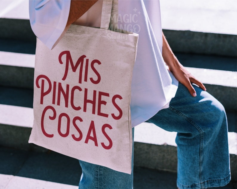 May include: A white canvas tote bag with the text "Mis Pinches Cosas" in red lettering.